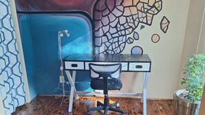 Un pequeño espacio de oficina con suelo de madera, un escritorio con una silla, una planta en maceta y un mural en la pared.