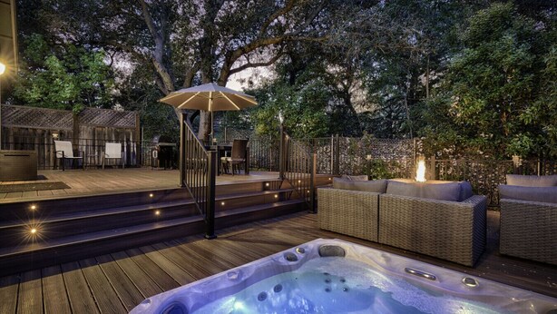 Un área de hidromasaje con terraza de madera, mobiliario exterior y una pérgola con luces.