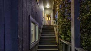 Una escalera de madera que conduce a una puerta con un panel de vidrio, rodeada de paredes de madera oscura y una barandilla de madera.