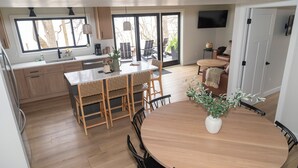 Une cuisine moderne avec des meubles en bois, un coin repas doté d’une table ronde et une porte-fenêtre coulissante donnant sur une terrasse.