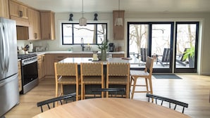 Une cuisine moderne avec des meubles en bois, un réfrigérateur en acier inoxydable et un coin repas comprenant une table et des chaises en bois.