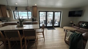Une cuisine moderne dotée d’un grand îlot central, de chaises en bois, d’une table à manger et d’un coin salon confortable avec un canapé et un téléviseur.