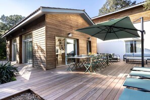 A wooden house with a deck, outdoor seating, and a large umbrella. - Villa Bikiak in the heart of Moulleau near the beach (Arcachon)