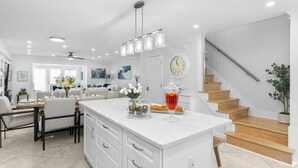 A modern kitchen with a large island, wooden staircase, and a dining area with a view of the living room. - Luxurious Townhome/Beach Access/11 Pools (Panama City)