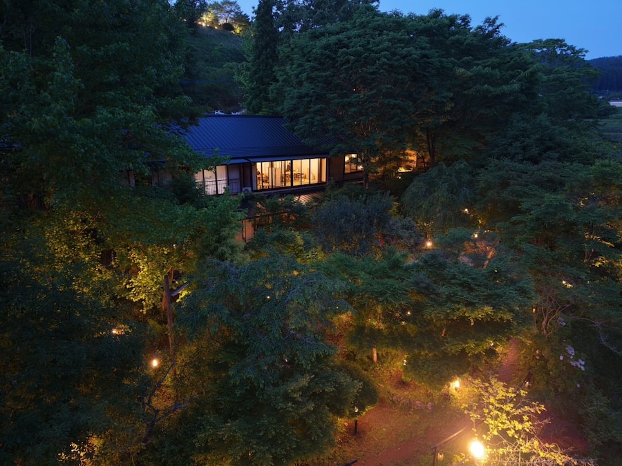 Una casa apartada rodeada de un bosque frondoso, con un sendero que lleva a la entrada.