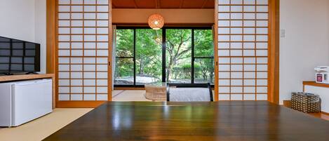 A traditional Japanese room with tatami flooring, a television, and a view of a garden through a shoji screen.