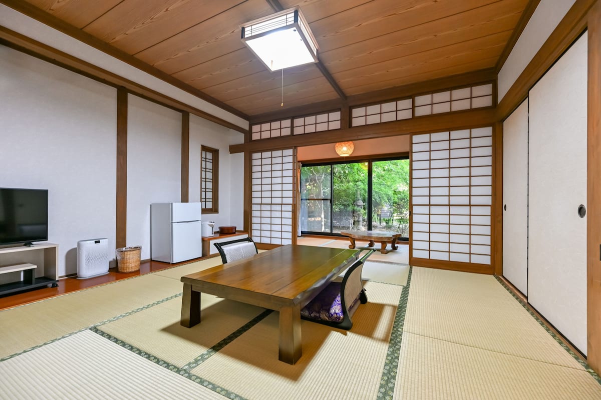 Een traditionele Japanse kamer met tatami vloerbedekking, een houten tafel, een televisie en schuifdeuren.