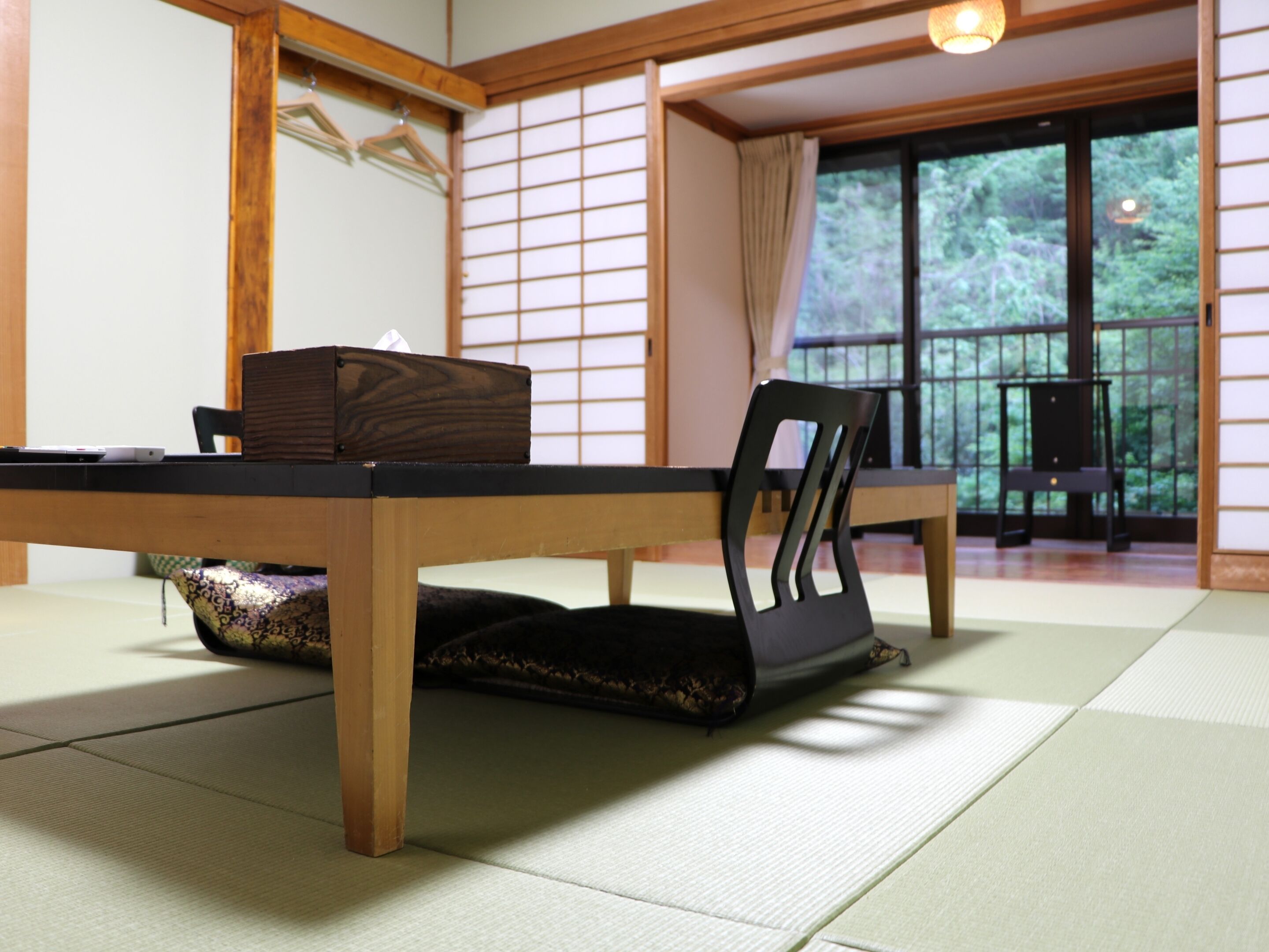 A traditional Japanese tatami mat room with a low table, a black chair, and a wooden cabinet.
