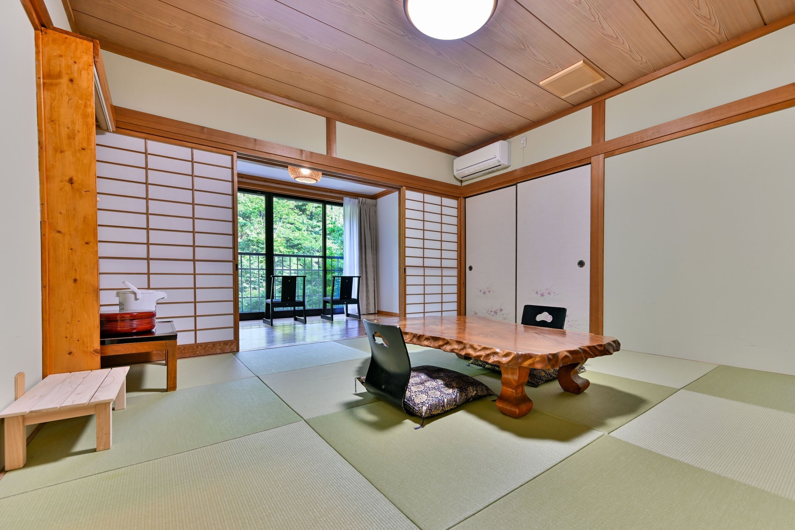 Une pièce de style japonais traditionnel, avec un sol recouvert de tatamis, une table basse, une chaise et une porte coulissante donnant sur un espace extérieur.