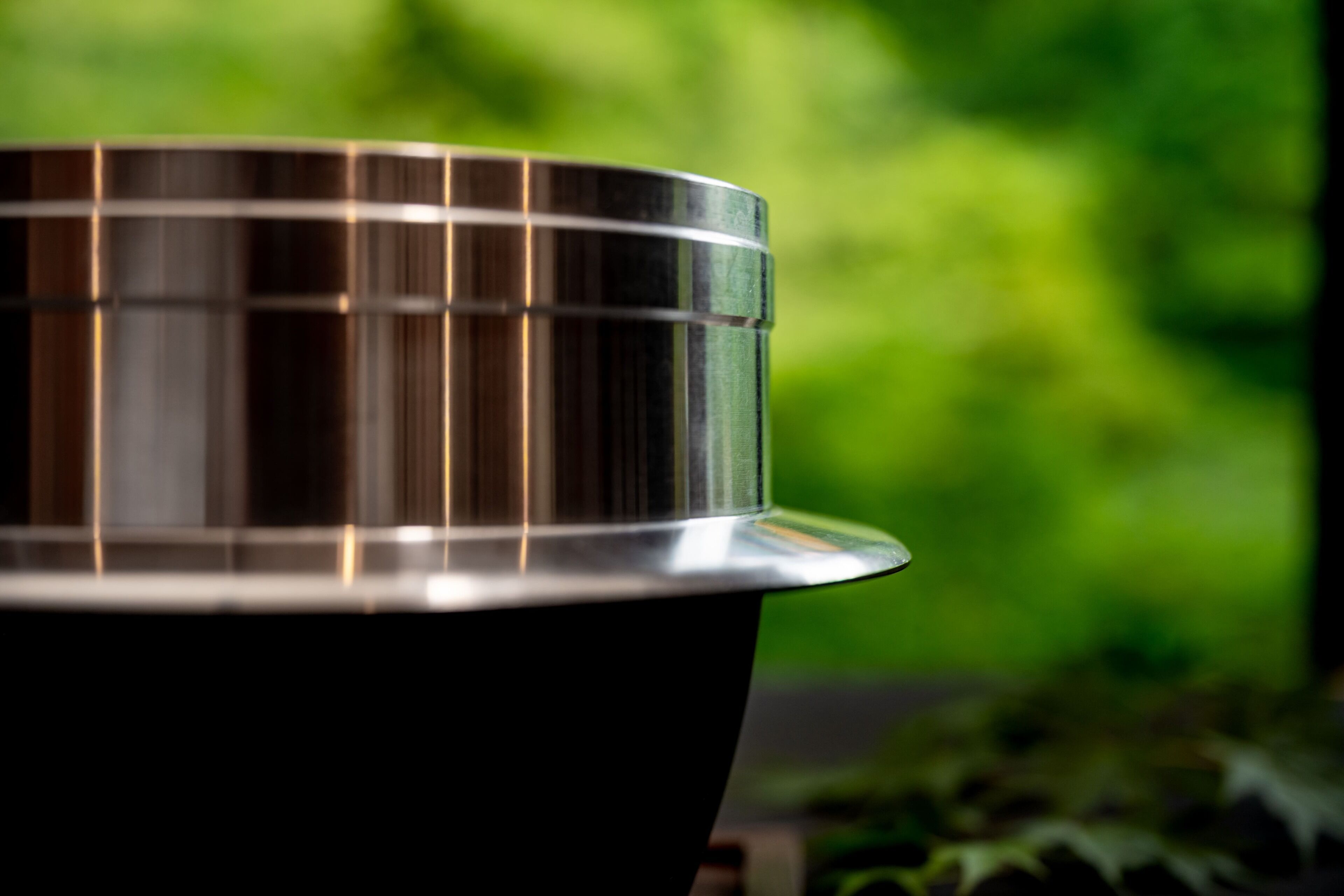 A metallic object with a reflective surface, possibly a part of a piece of furniture or equipment, set against a blurred green background.