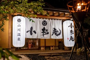 Un edificio japonés tradicional con fachada de madera, un sendero de piedra y faroles colgantes.