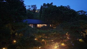 Une maison entourée d’arbres, illuminée à la tombée de la nuit.