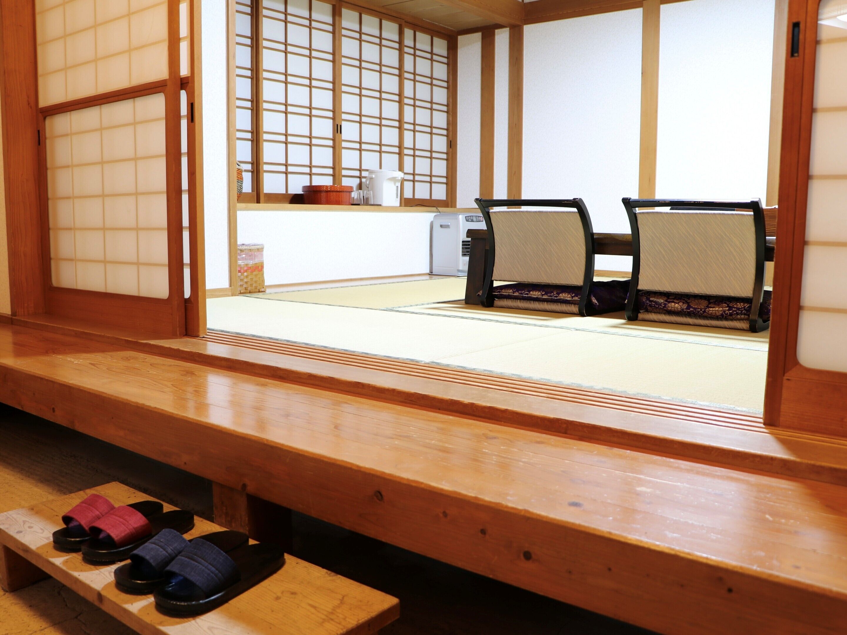 A traditional Japanese room with tatami flooring, a low wooden table with slippers, and a sliding door with a grid pattern.