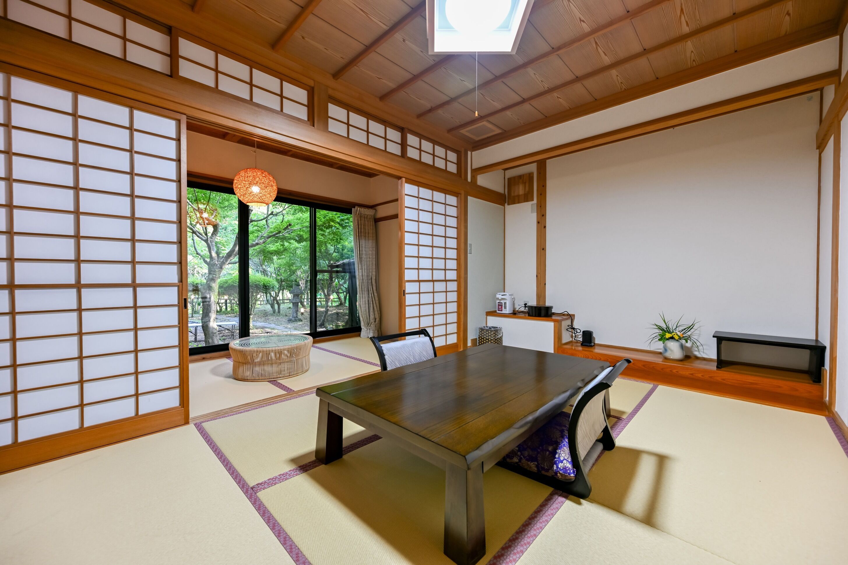 Une pièce de style japonais traditionnel, avec un sol recouvert de tatamis, une table basse, des portes coulissantes et une vue sur la verdure à l’extérieur.