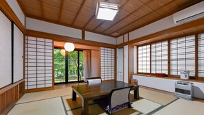 Une pièce de style japonais traditionnel, avec un sol recouvert de tatamis, une table basse en tatami, des portes coulissantes et une vue sur la verdure à l’extérieur.