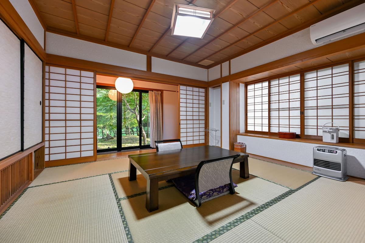 Een traditionele Japanse kamer met tatami vloeren, een laag tafeltje van tatami strooisel, glijdende deuren en uitzicht op groen buiten.