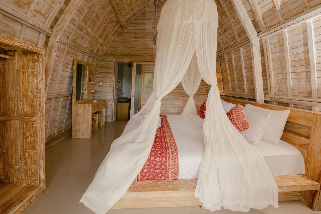 Una habitación de madera con una cama bajo un dosel, un banco de madera y un espejo en la pared.