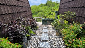 Un sentier qui traverse un jardin, bordé d’une clôture en métal et agrémenté d’une porte décorative, et qui est entouré de diverses plantes et fleurs.