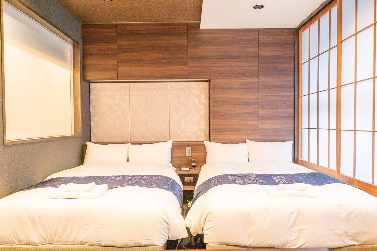 Een hotelkamer met twee bedden, een houten hoofdeinde, een nachtkastje en een groot raam met uitzicht.
