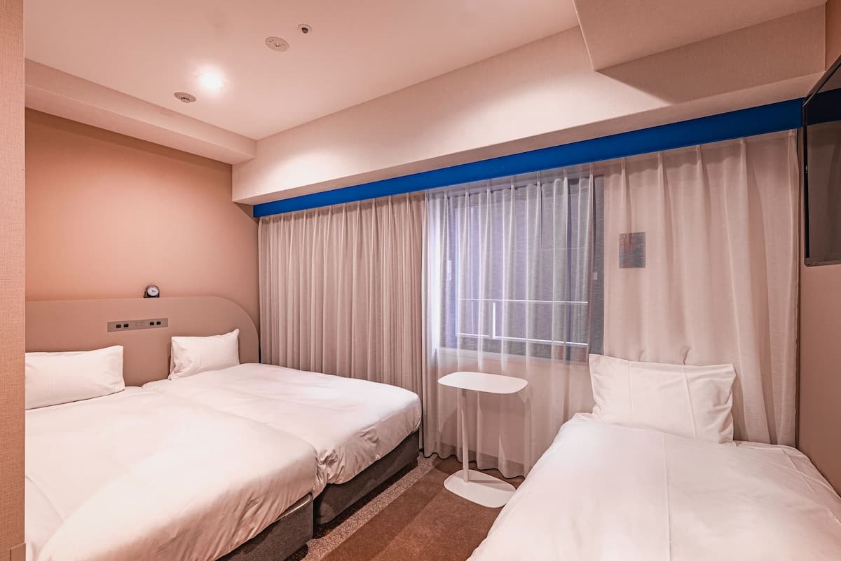A hotel room with two beds, a small round table, and a large window with sheer curtains.