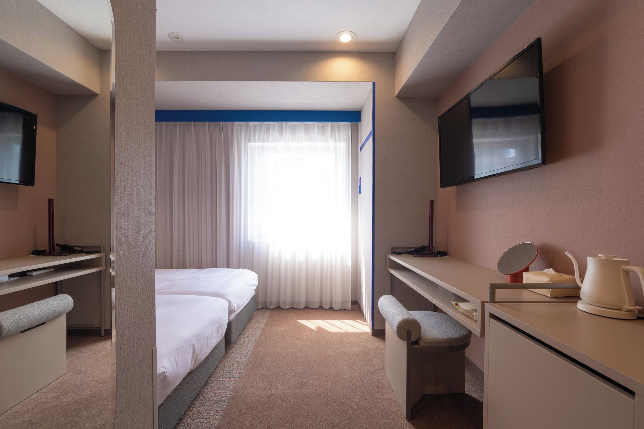 A hotel room with a bed, a desk, a chair, a TV, and a window with curtains.