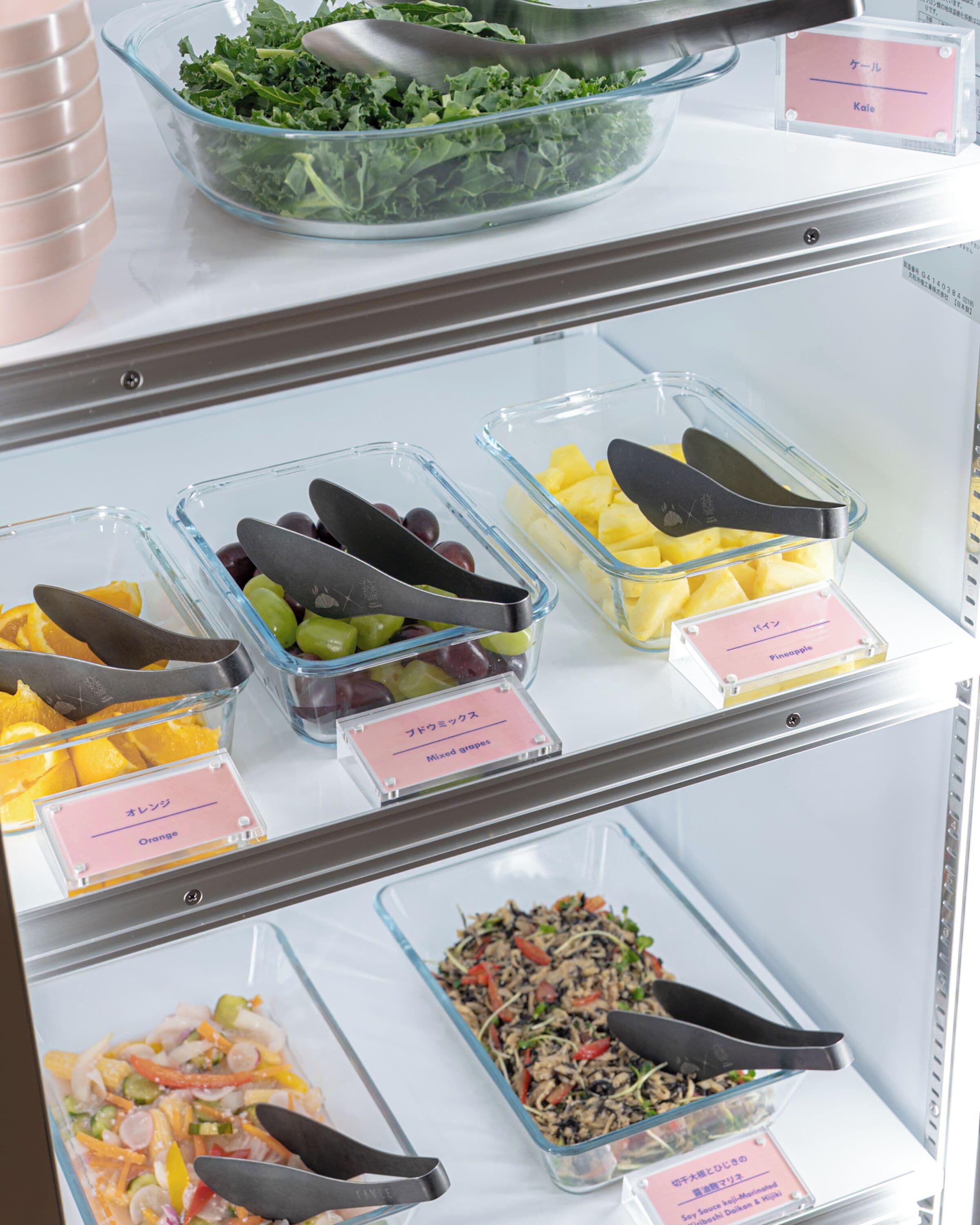 Een gekoelde display vitrine met verschillende etenswaren, waaronder druiven, ananas, oranjeschijfjes en een salade.