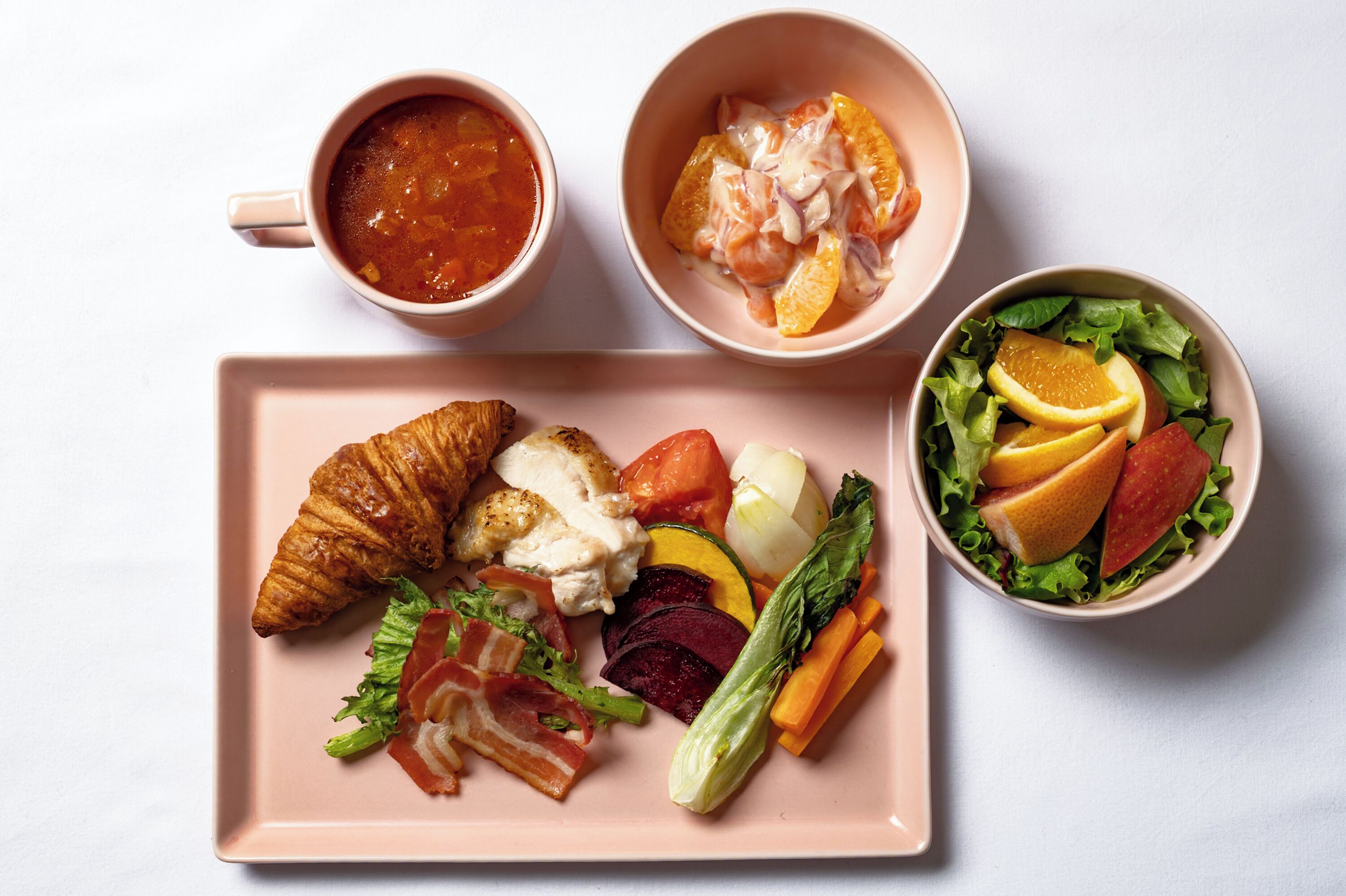 A breakfast setting with croissants, eggs, vegetables, and fruit.