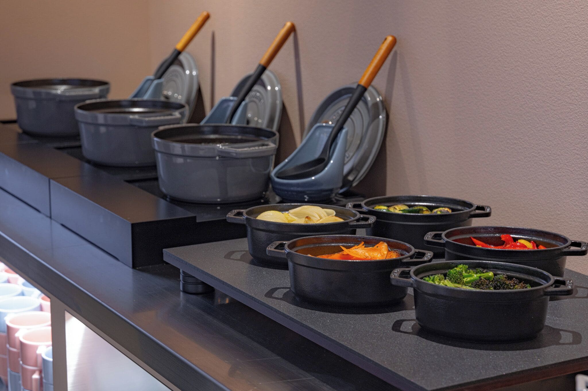 Eine Speiseauswahl vom Buffet mit verschiedenen Gerichten in schwarzen Töpfen, darunter Gemüse und möglicherweise Fleisch.