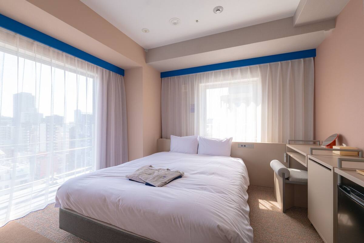 A hotel room with a bed, a desk, and a view of the cityscape.