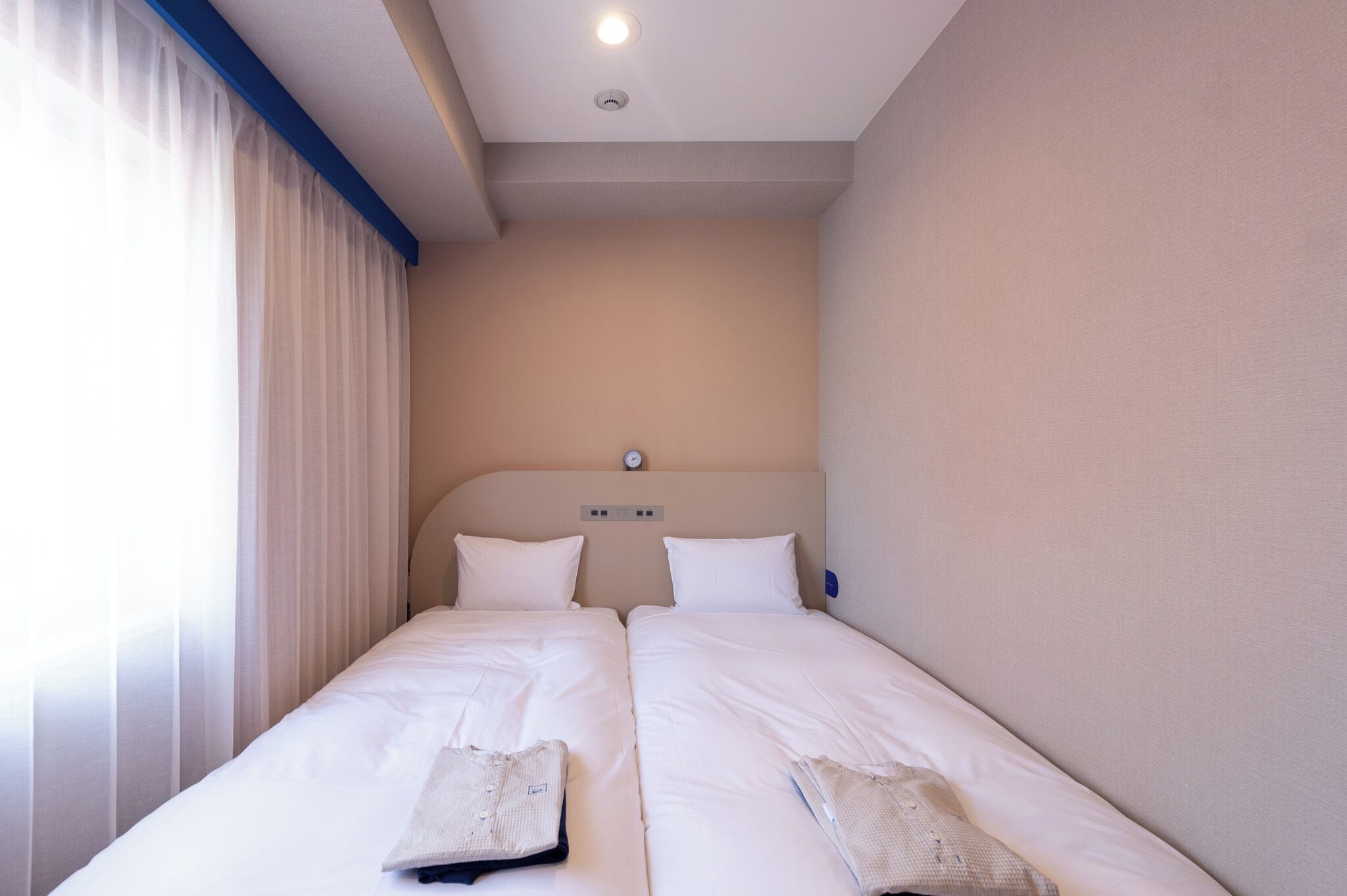 Een hotelkamer met twee bedden, een plafondlamp en een raam met gordijnen.