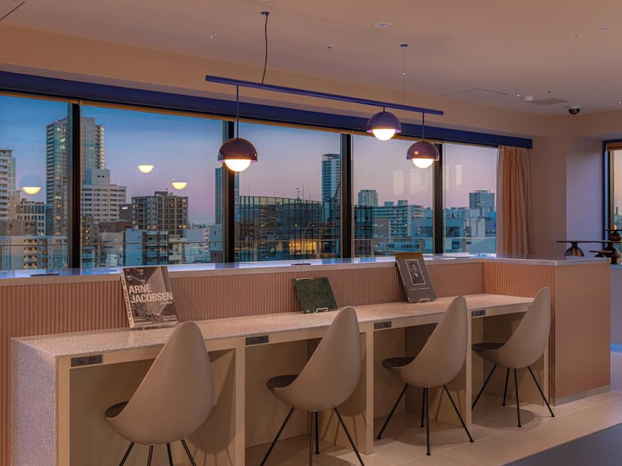 A modern hotel lobby with a city view, a reception desk, and seating area.