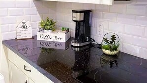 A kitchen with a coffee maker, a coffee bar sign, a small plant, and a glass container with plants.