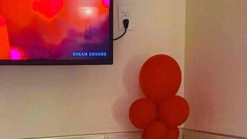 A bathroom with a bathtub, red balloons, candles, and rose petals on the floor.