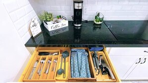 A kitchen with a coffee maker, a coffee bar sign, and utensils in a drawer.