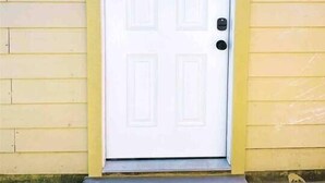 A white door with a rectangular panel design, flanked by yellow siding walls, and a small step leading to the door.
