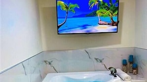 A bathroom with a marble bathtub, a television mounted above it, and a small shelf with toiletries.