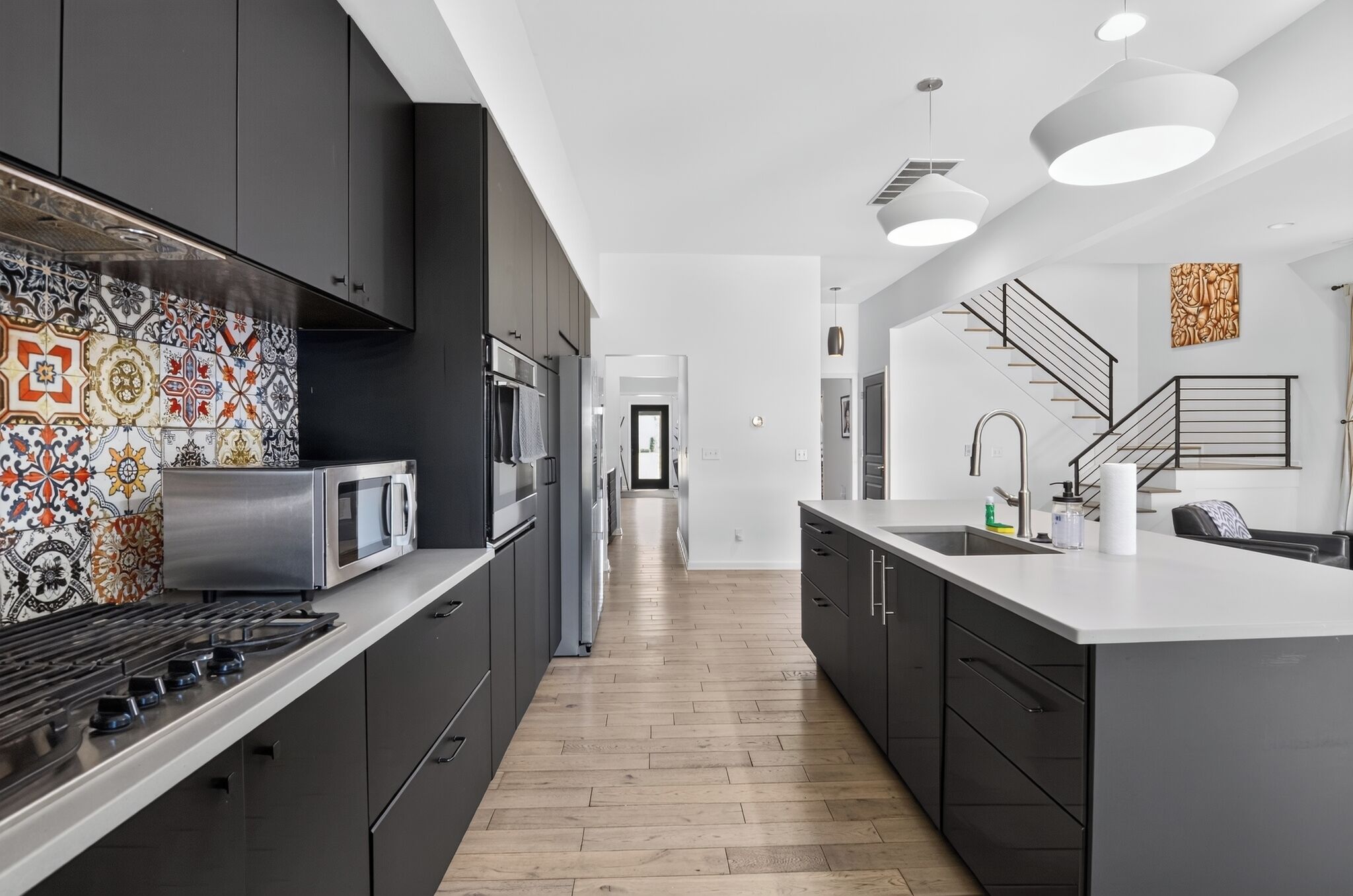 A modern kitchen with dark cabinetry, a patterned backsplash, a central island, and a staircase leading to another level.