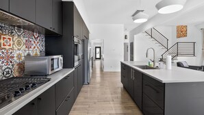 Una cocina moderna con armarios oscuros, un salpicadero estampado, una isla central y una escalera que sube a otro nivel.