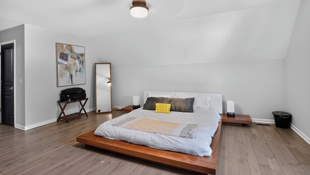 Un dormitorio con cama, mesitas de noche, ventilador de techo, espejo y un cuadro en la pared.