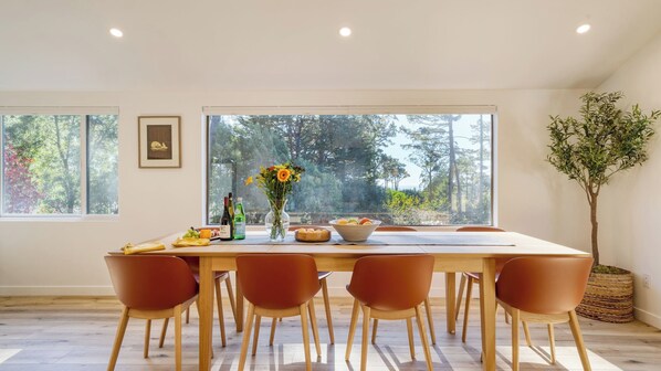 Un coin repas avec une grande fenêtre, une table dressée avec de la nourriture, des boissons et un vase de fleurs.