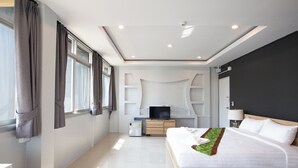 Une chambre d’hôtel moderne équipée d’un grand lit, d’une télévision, d’un petit réfrigérateur et d’un bureau avec une lampe.