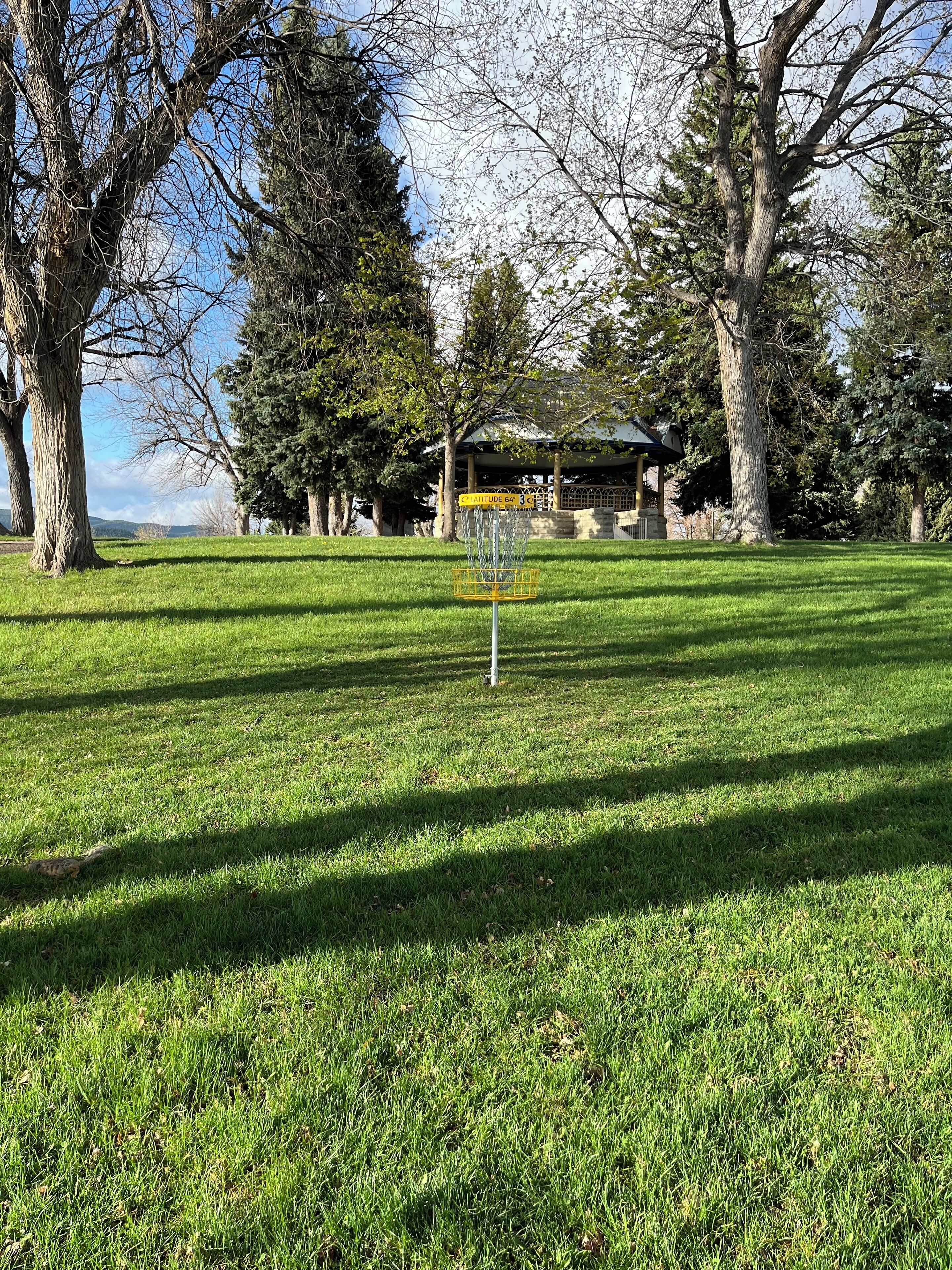 Ein gepflegter Rasen mit einem Disc-Golf-Korb und einem Schild, das eine Entfernung von 64 Metern angibt.