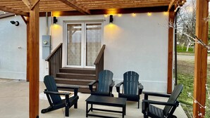 A covered patio with wooden beams, a concrete floor, and a set of Adirondack chairs and a small table. - Kit Carson Bungalow: AC/Heat + Pets Free! (Trinidad)