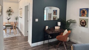 A modern living room with a dark accent wall, a dining area with a wooden table and chairs, and a large mirror above a desk. - Kit Carson Bungalow: AC/Heat + Pets Free! (Trinidad)