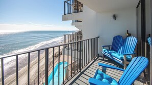 Un balcon avec vue sur l’océan, des chaises bleues et une piscine.