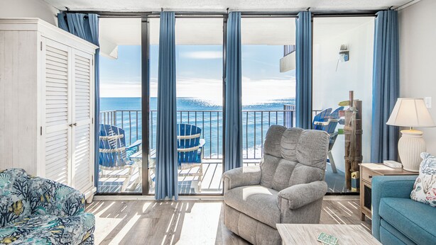 Un balcon avec vue sur la mer, un fauteuil gris, un canapé bleu et un plancher en bois.