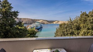 Een balkon met een tafel, een bloempot en uitzicht op een boot op een meer met heuvels op de achtergrond.