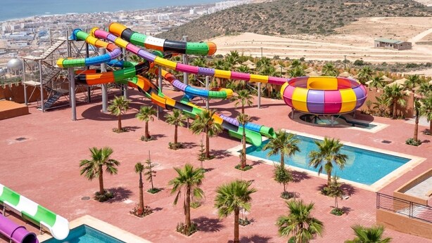 Parc aquàtic amb diverses tobogans i una banyera d'hidromassatge, envoltat de palmeres i una piscina.