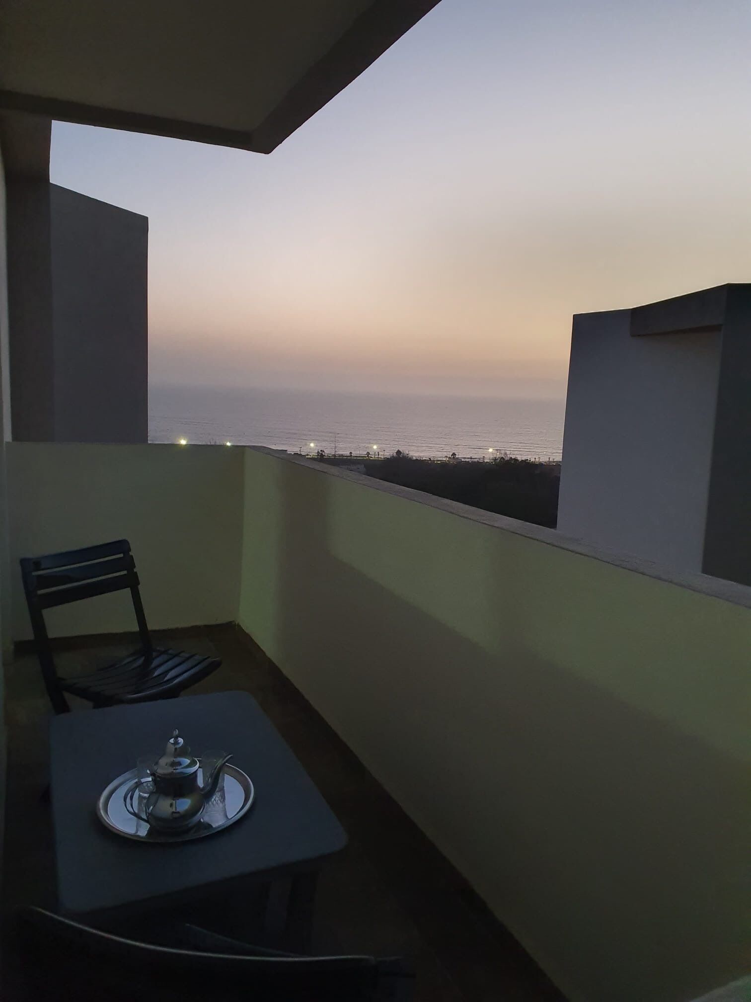 Un balcon avec une table et une chaise, donnant sur une étendue d’eau au crépuscule.