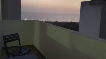 Un balcon avec une table et une chaise, donnant sur une étendue d’eau au crépuscule.